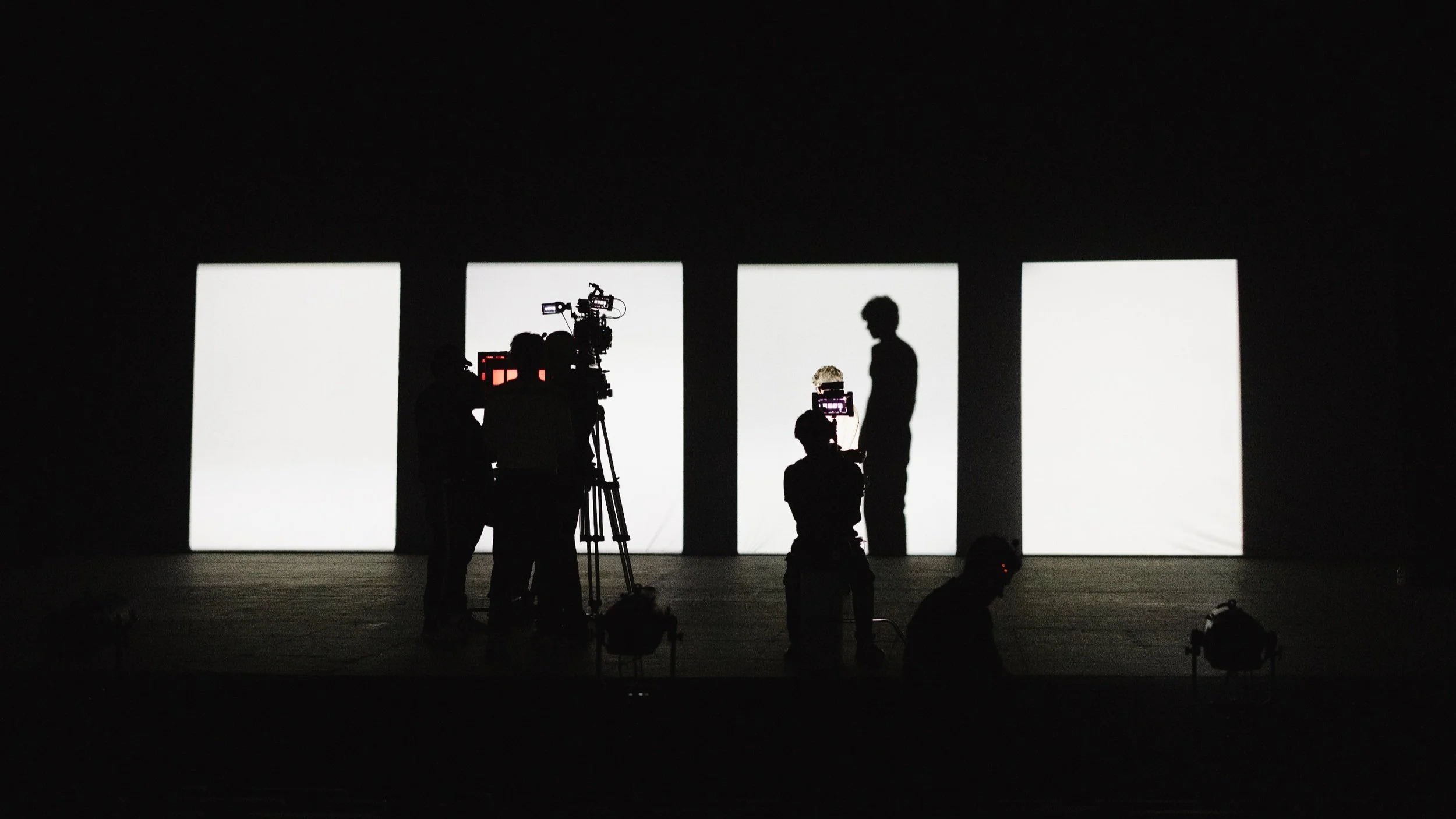 Film crew and cameras silhouetted against studio lights